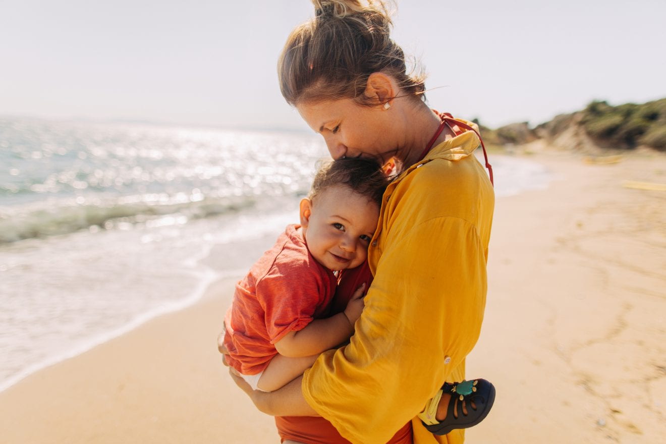 Photo of mother hugging her baby boy while enjoying together at the beach