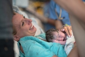 A mother smiles as she holds her newly born infant for the very first time on her chest.