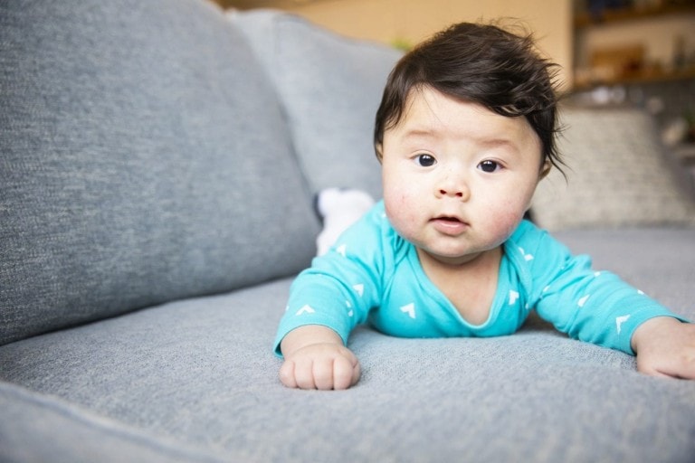 Young Chinese American baby boy laying on his tummy on the couch.