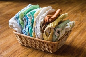 A display of varying colors, shapes and sizes of cloth diapers arranged in a small rectangle shaped basket on a wooden surface.