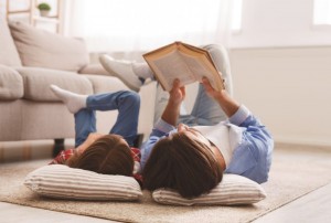 Little daughter and daddy enjoying time together, laying on floor at home, man reading book to his cute daughter.