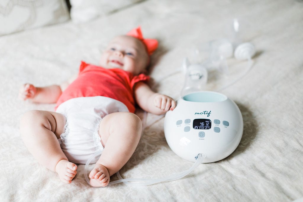 Baby laying on a bed next to the Motif Luna breast pump.