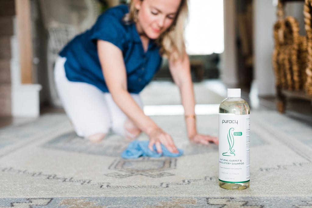 A woman using Puracy Natural Carpet Cleaner to spot clean her rug.
