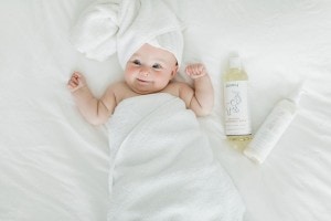 Baby wrapped up in a towel laying on the bed with Puracy natural baby products