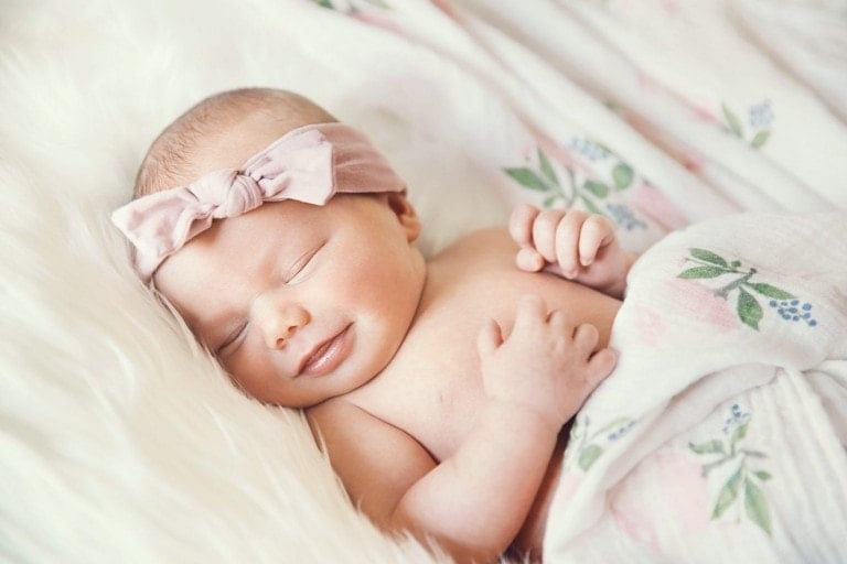 Sleeping newborn baby in a wrap on white blanket. Beautiful portrait of little girl, one week old. Baby smiling in a dream.