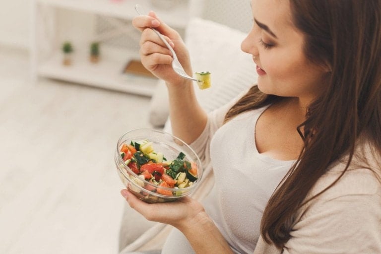 Young pregnant woman eating green salad.