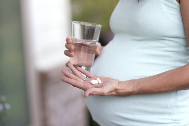 Adult pregnant woman about to swallow vitamins with water