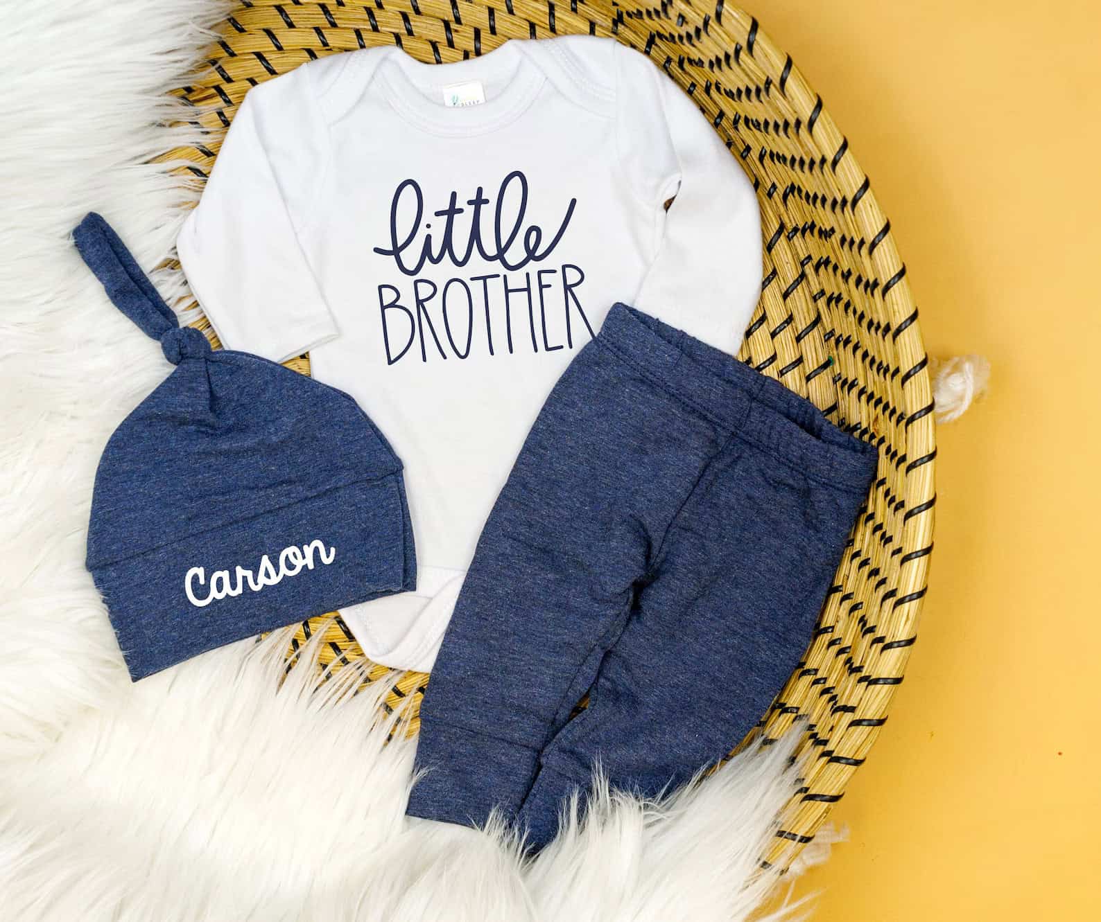 Little brother coming home outfit featuring a white onesie with "Little Brother" written on it, navy blue pants, and a matching navy monogrammed hat