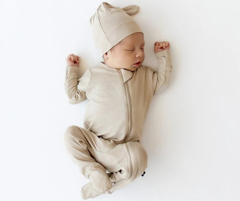 A baby wearing the Kyte Baby Zippered Footie in Almond