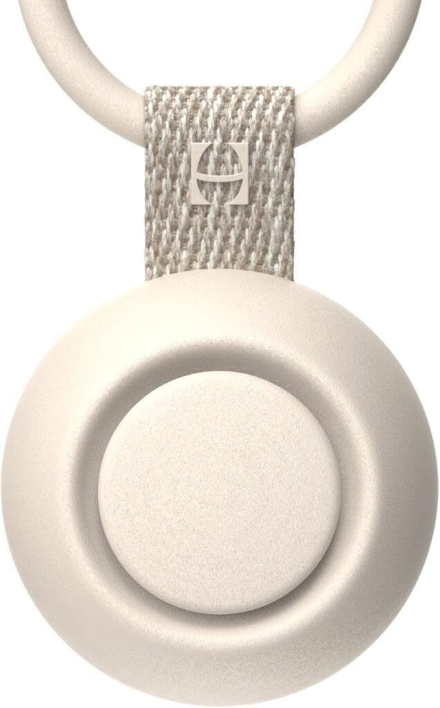 A close-up image of a beige circular device, perfect as a thoughtful gift to bring a new family, with a textured loop at the top featuring a small square logo. The device appears smooth and slightly rounded.