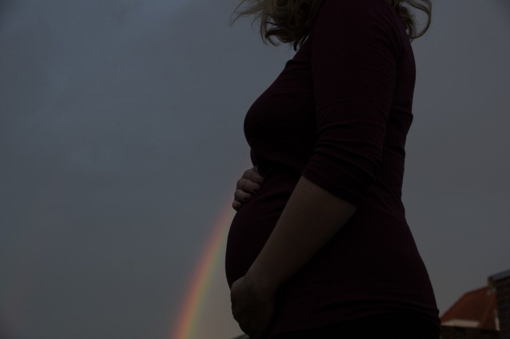 Pregnant woman in perspective with a rainbow representing her rainbow baby.