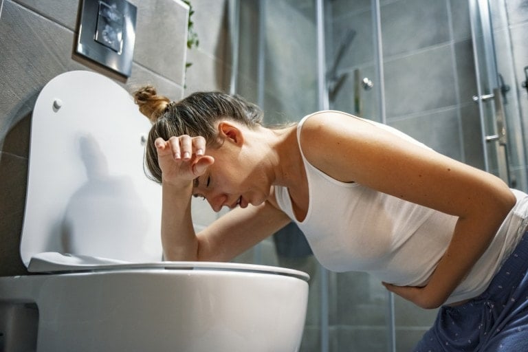 Young caucasian woman with her hair up in a bun kneeling over the toilet sick due to morning sickness during pregnancy.