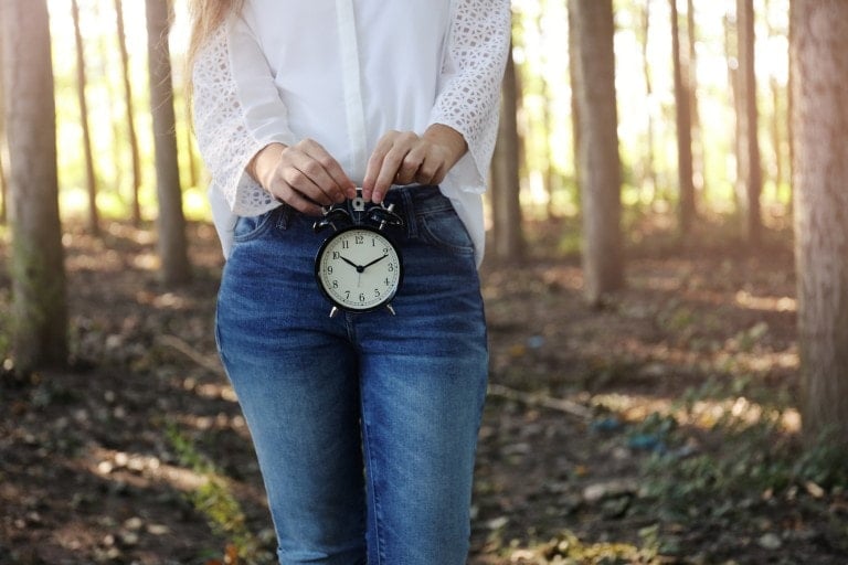 Woman with alarm clock in the woods.
