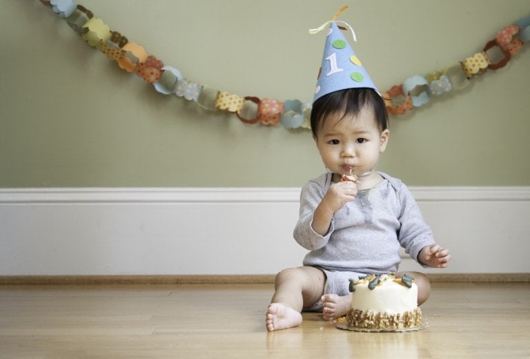 Asian baby celebrating his First Birthday in front of his birthday cake at his birthday cake smash photoshoot. He's putting the birthday candle into his mouth.