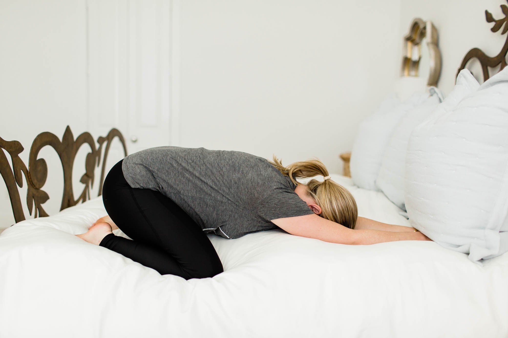 Pregnant woman doing child's pose on her bed.