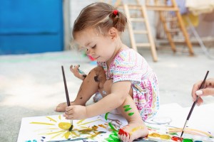 Cute little caucasian Girl enjoying Painting at the backyard with paper, water color and art brush.