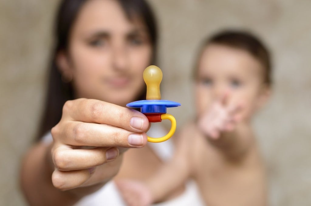 mother shows Pacifier while holding the baby