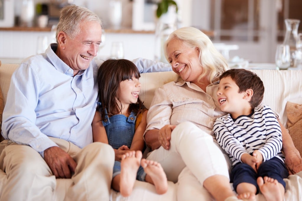 White senior couple and their grandchildren sitting on a sofa together smiling at each other.