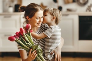 A young son giving his mother a bouquet of pink tulips and giving her a kiss on the cheek.