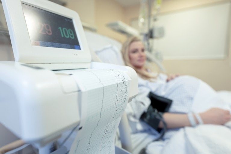 Pregnant woman in the labor and delivery room at the hospital, sitting on the bed in labor getting her blood pressure checked and fetal monitors on.