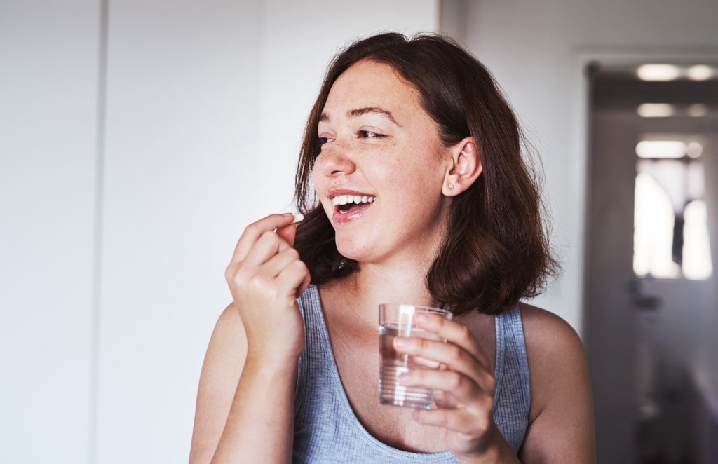 Cropped shot of a young woman taking supplements at home.
