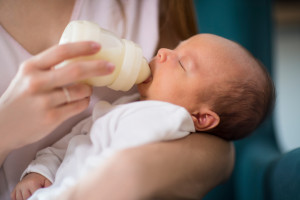 Close Up Of Loving Mother Feeding Newborn Baby Son With Bottle At Home