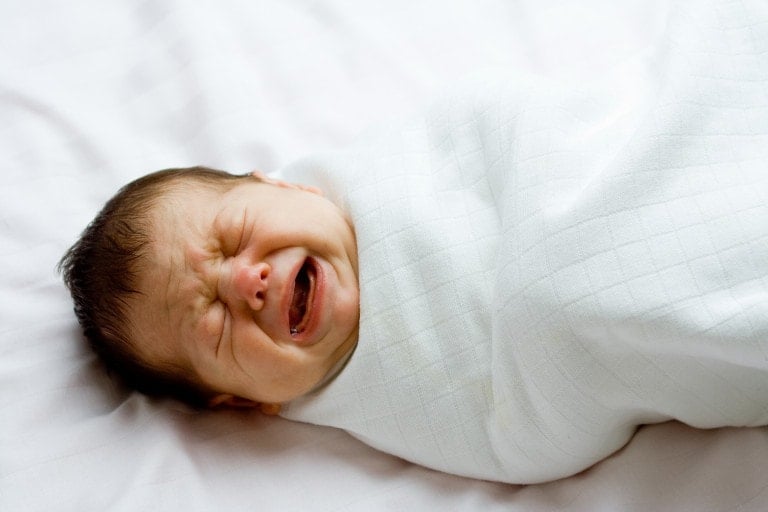 Crying newborn infant in white blanket.