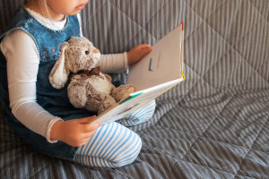 Little girl reading favorite book at home with her toy rabbit.