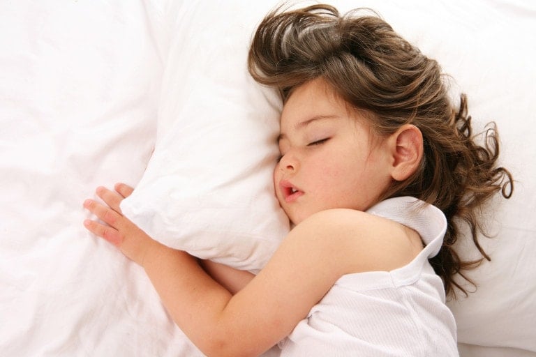 Little girl sleeping on a white bed with her pillow