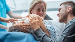 In the Hospital Midwife Gives Newborn Baby to a Mother to Hold, Supportive Father Lovingly Hugging Baby and Wife. Happy new Family in the Modern Delivery Ward.