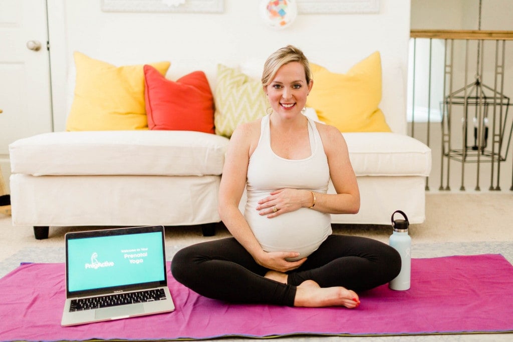 Pregnant woman sitting on the floor on her yoga mat with her computer on PregActive workout.
