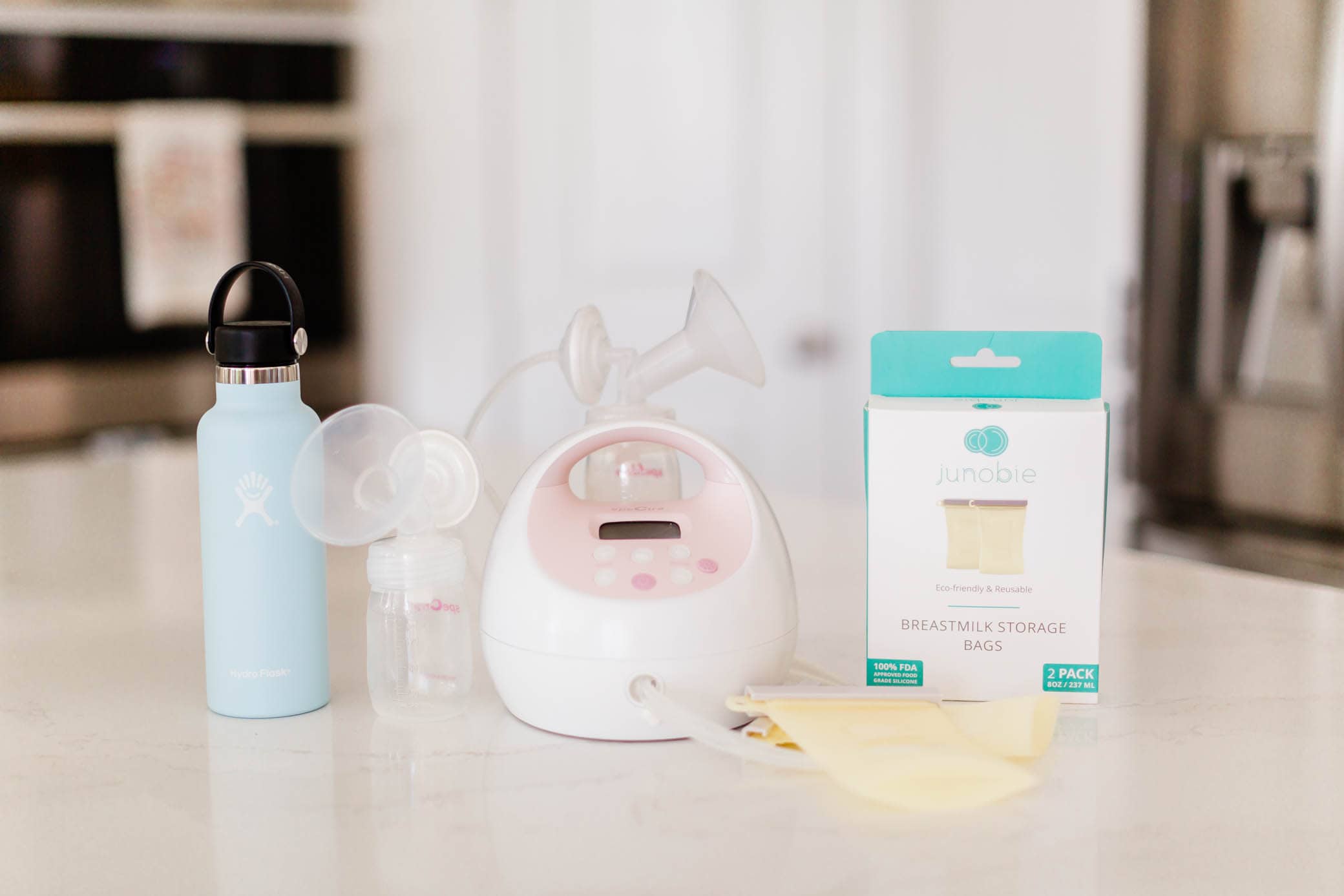Breast pump, water bottle, and Junobie breastmilk storage bags on a kitchen counter
