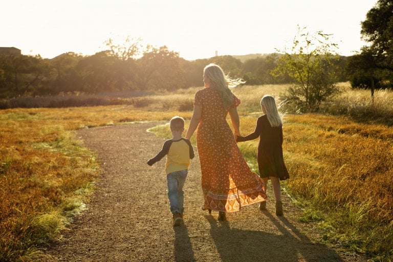 Young widow mother holding her children's hands as they walk off into the sunset.