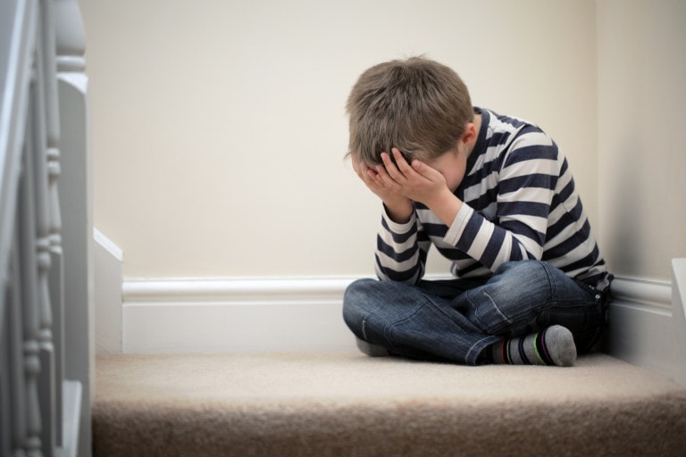 Upset child with head in hands sitting on staircase.