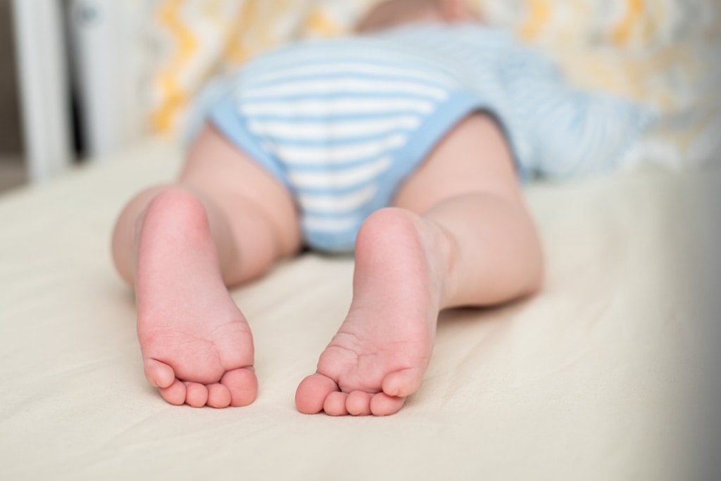 Legs of a sleeping baby on his abdomen in his crib. Infant's feet.