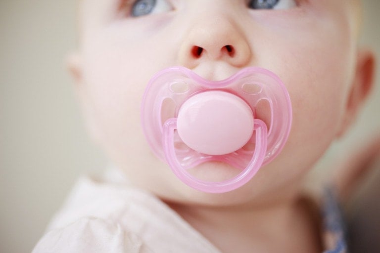 Close up photo of a little girl sucking a pink pacifier.