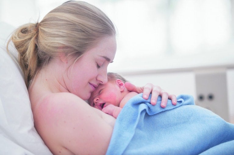 A mother is cradling her newborn baby. They are indoors in a hospital room.