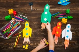 the child holds the rocket made of paper against the background of a wooden table. preschool Child in creativity in the home.