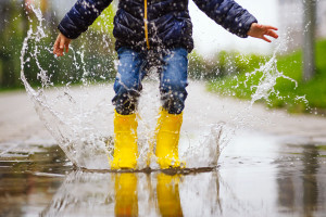 Close up legs of child with yellow rubber boots jump in puddle on an autumn walk