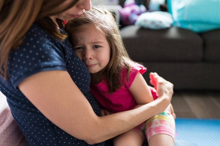 Mother consoling crying adorable girl while sitting in living room at home