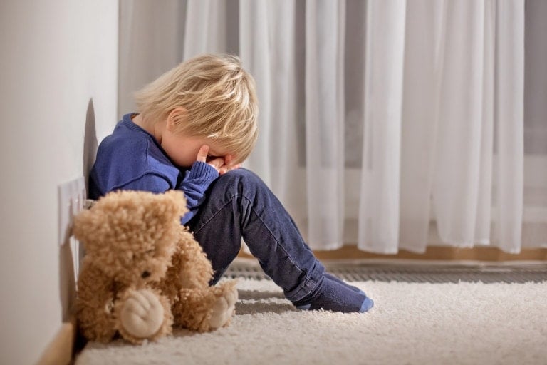 Sad little toddler child, blond boy, sitting in corner with teddy bear, punished for mischief