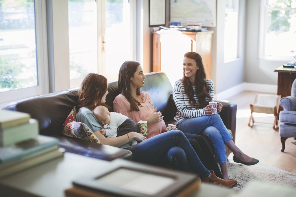 Pregnant woman and female friends talking while sitting on sofa.