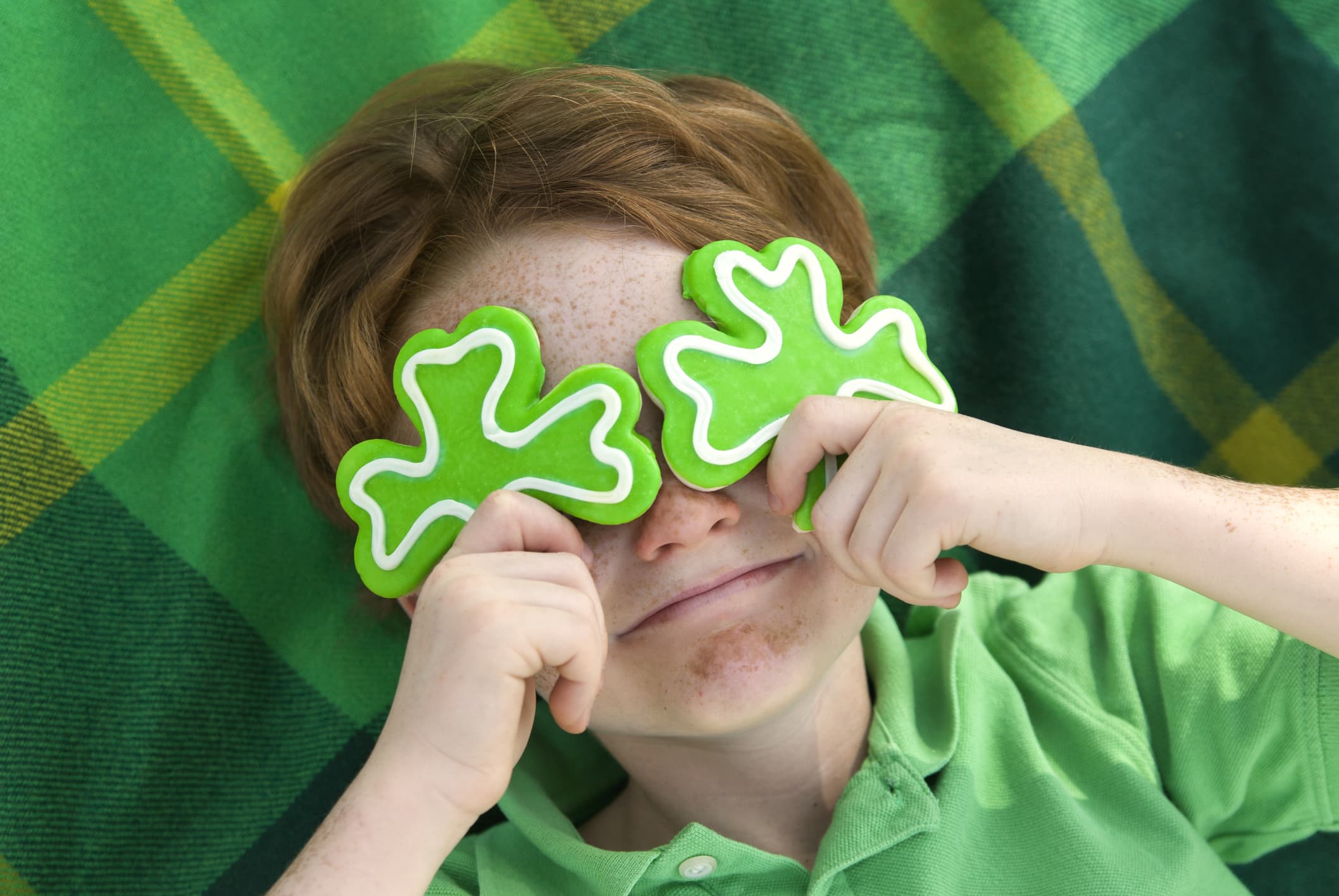 Redhead and freckle face Irish boy leprechaun with shamrock cookies over his eyes.