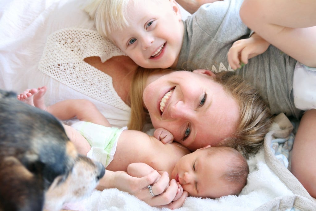 Happy Young Mother Laying in Bed with Toddler Son and Newborn Baby Daughter