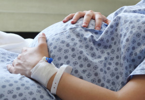 Pregnant woman wearing a hospital gown with her hands around her bump.