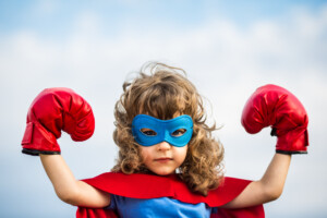Superhero kid wearing boxing gloves against blue sky background.