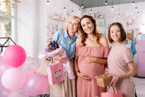 Three women smiling while celebrating a friend's pregnancy at her baby shower.