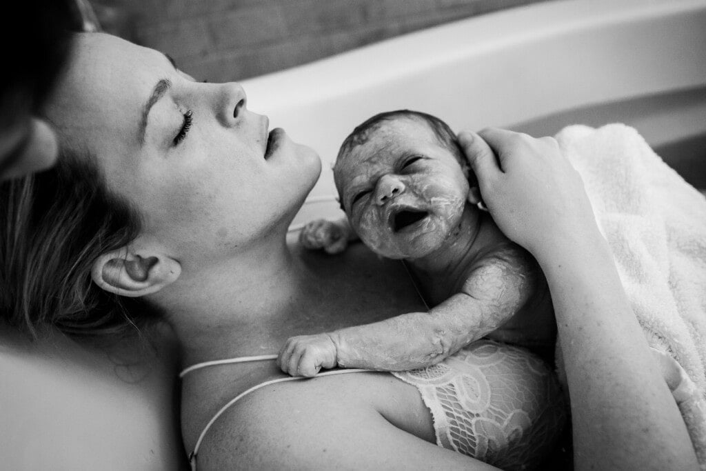 Woman laying in a tub with her new baby on her chest.
