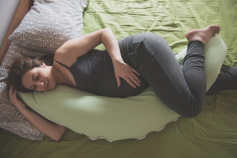 Pregnant woman feeling pain in abdomen while laying down with her pregnancy pillow.