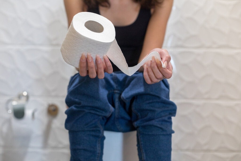 Woman sitting in the toilet holding toilet paper